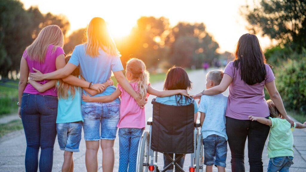 Group of adults and children walking together with a wheelchair user at sunset. NDIS Community Access Gold Coast | Loving Hearts
