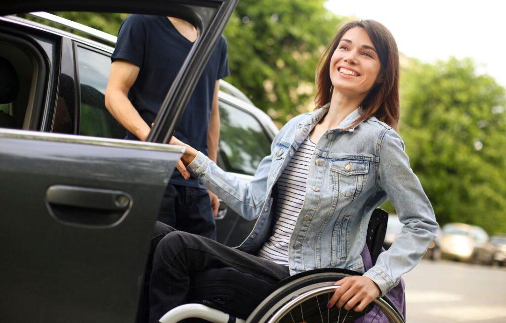 Woman using a wheelchair getting into a car with support nearby. NDIS Support Workers Gold Coast | Loving Hearts